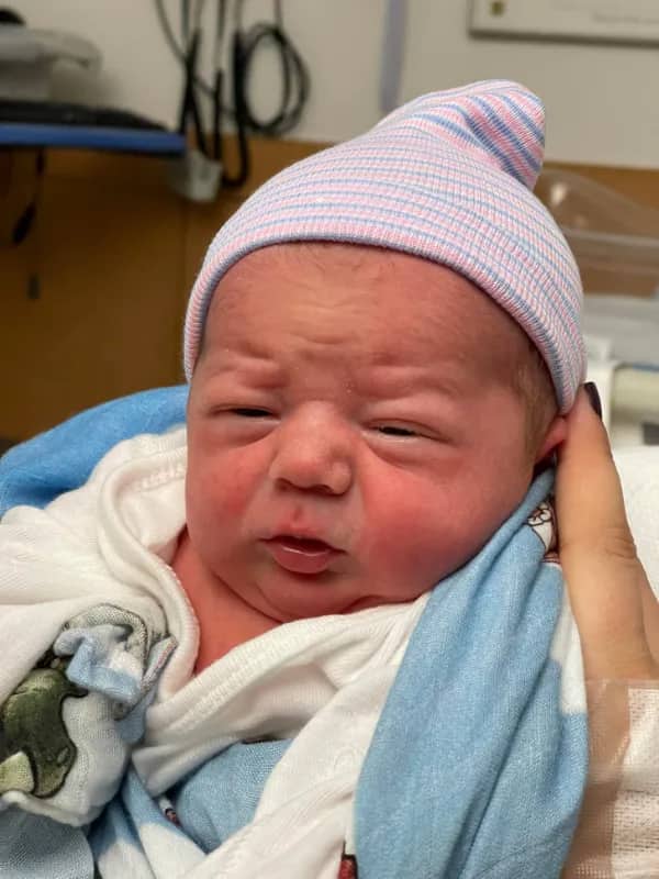 Swaddled newborn with a squint and double chin looking like a very tired 50 year old man.