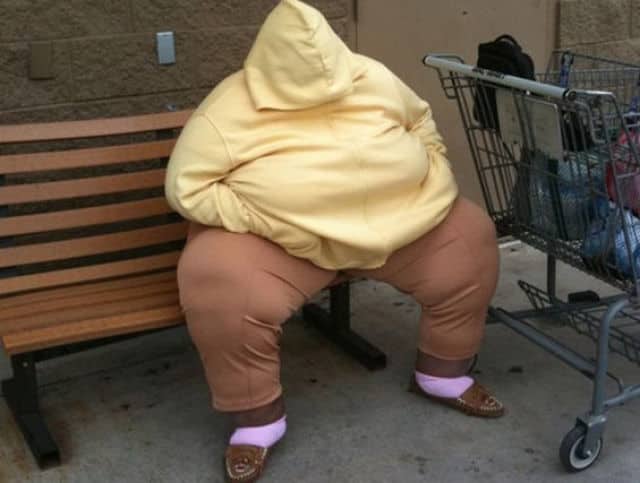 Person sitting on a bench wearing a yellow hoodie pulled completely over their face.