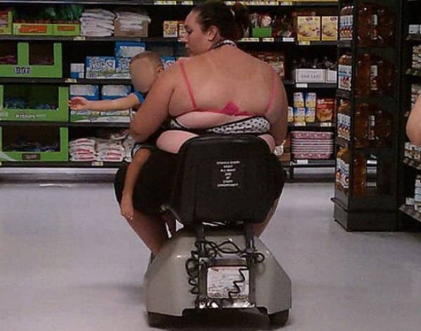 Woman on a mobility scooter holding a child with visible pink bra straps and midriff.