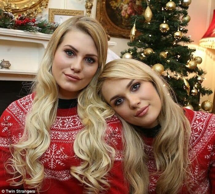 Two blonde women in matching red and white snowflake Christmas sweaters posing by a tree.