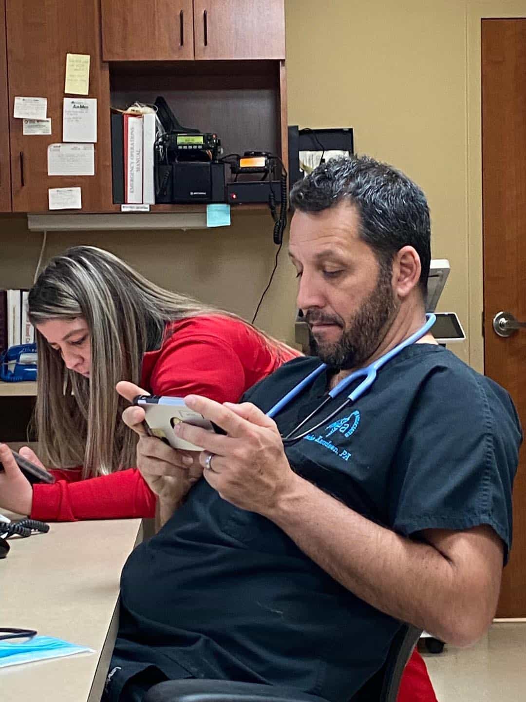 A medical professional in blue scrubs sitting at a desk, looking exactly like the famous actor.