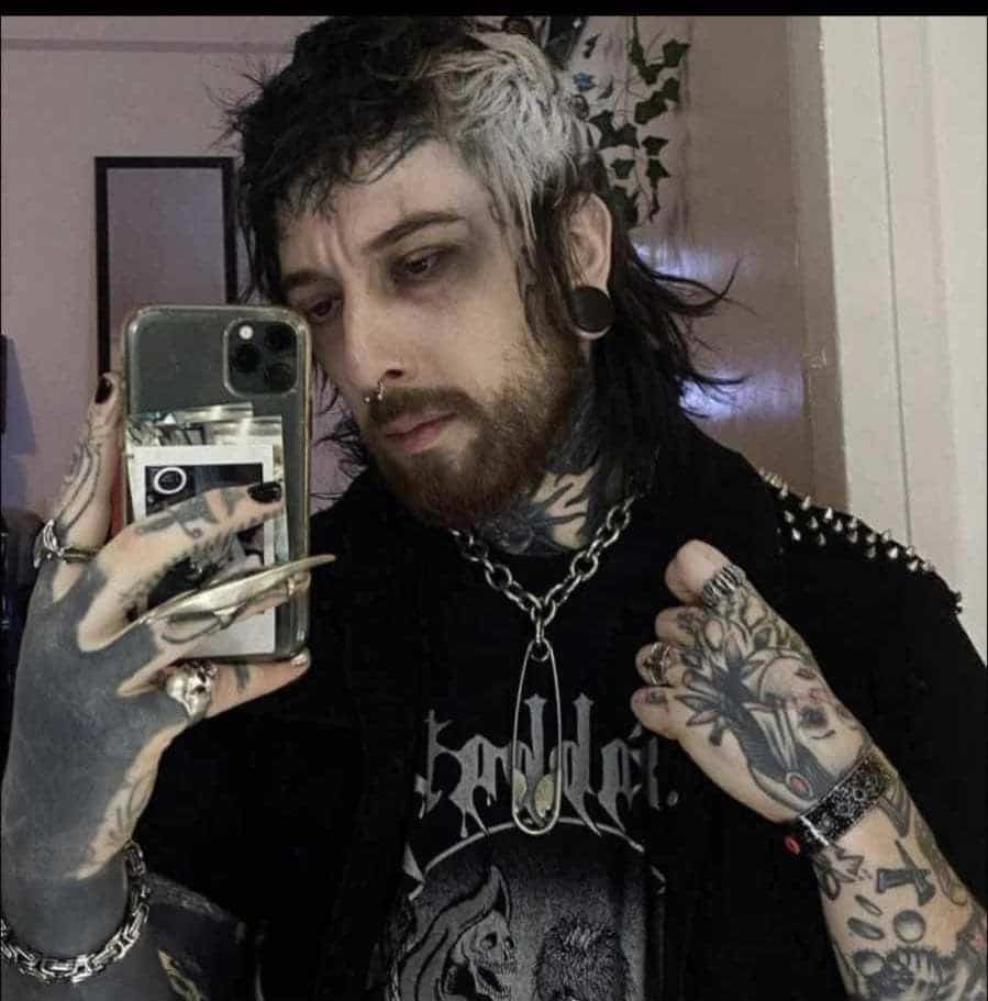 An edgy man with facial tattoos and black and white hair resembling a "goth" Adam Sandler.