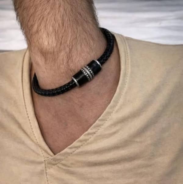 Close up of a man's neck featuring a thick black braided leather necklace with silver accents.