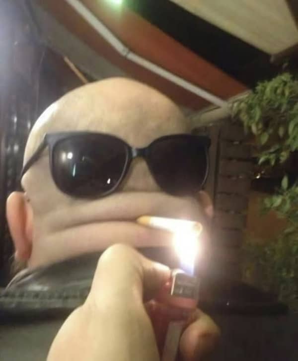 Back of a bald man's head with sunglasses and a cigarette placed in a skin fold.
