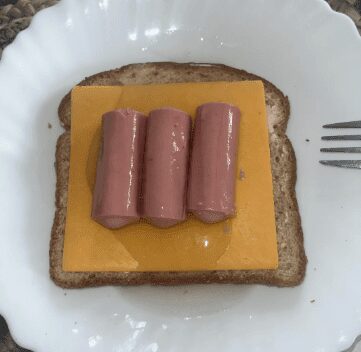 Three Vienna sausages served on a slice of American cheese and wheat bread on a white plate.