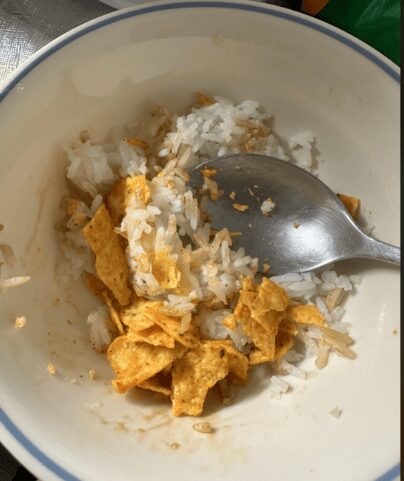 White bowl containing white rice mixed with crushed corn chips, representing a low-budget meal option.