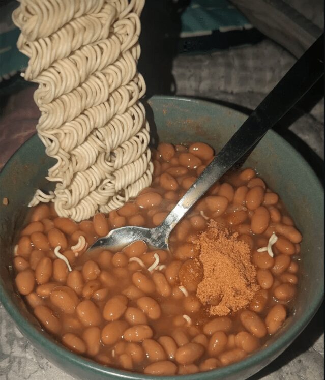 Bowl of baked beans topped with dry instant ramen noodles and a pile of seasoning powder.