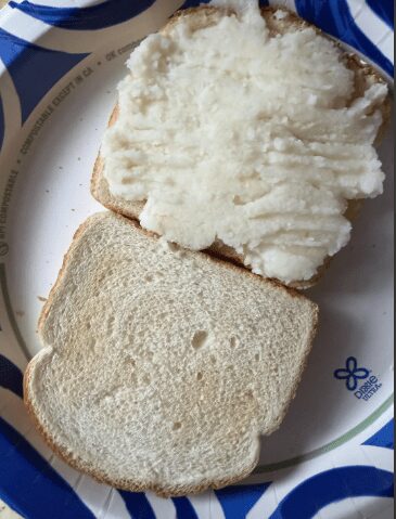 Two slices of white bread on a paper plate, one heavily spread with thick mashed potatoes.