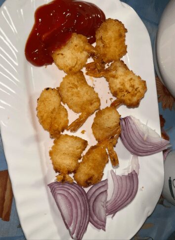 Breaded butterfly shrimp served with a large dollop of ketchup and raw red onion slices.