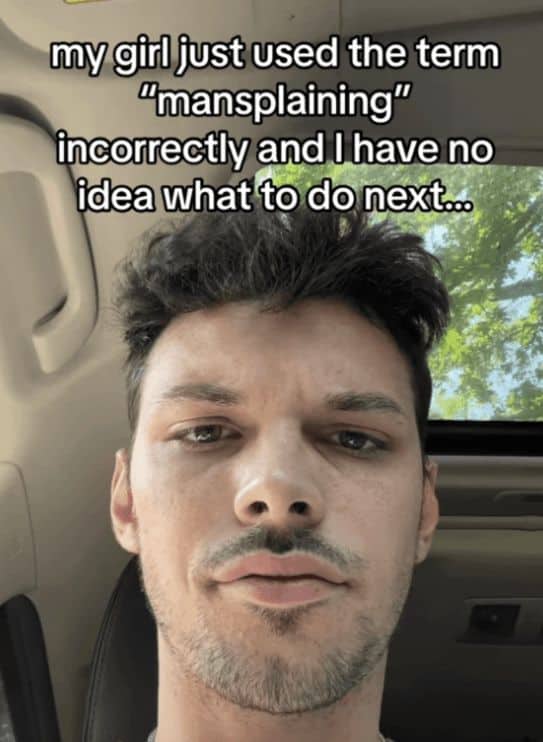 A selfie-style unhinged screenshot of a man looking directly into the camera with a deadpan expression. The caption highlights a bizarre relationship dilemma: "my girl just used the term 'mansplaining' incorrectly and I have no idea what to do next..."