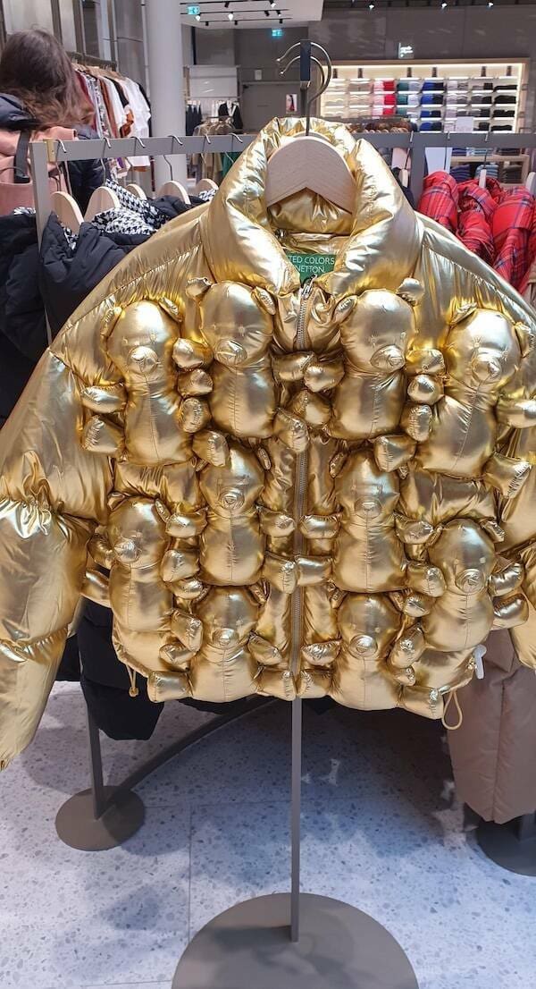 A high-shine metallic gold puffer jacket that takes "cluttercore" to the extreme, with dozens of small, stuffed teddy bears sewn directly onto the front and sleeves.