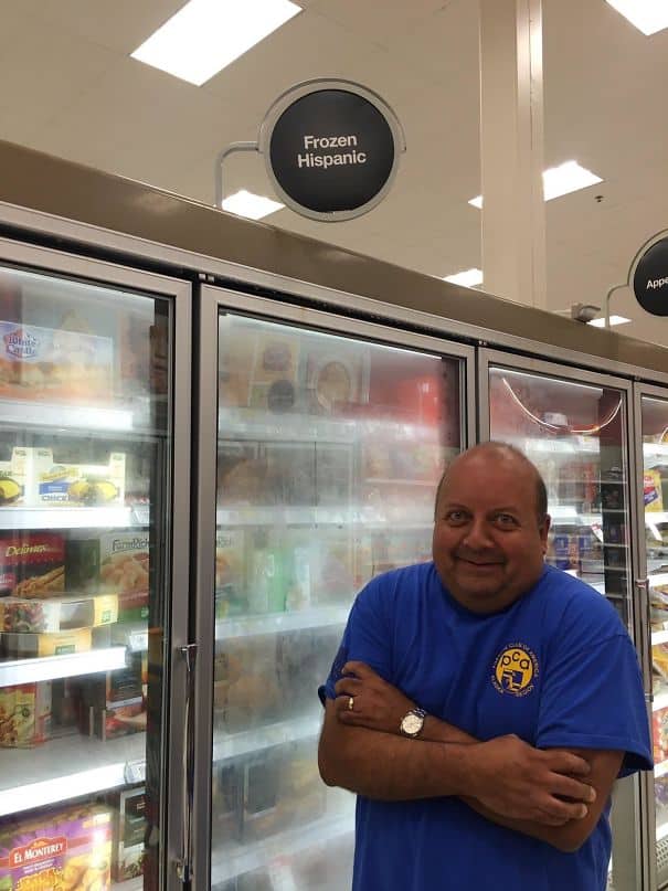 Man standing in front of a grocery freezer labeled Frozen Hispanic with a smirk.