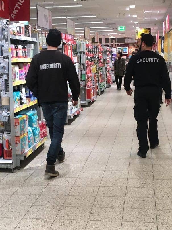 Two men walking in an aisle, one wearing a Security shirt and one wearing Insecurity.
