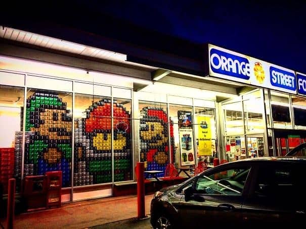 Storefront windows decorated with pixelated Mario and Luigi figures made from stacked colorful soda cases.