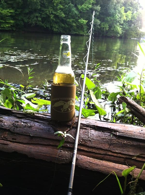 peaceful wholesome image of a fishing rod and a cold drink resting on a fallen log by a quiet, sun-dappled river, perfectly capturing the essence of a slow, meditative afternoon in nature.