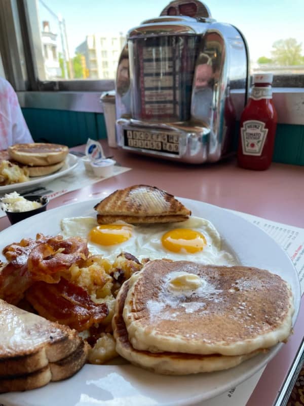 comforting wholesome image of a classic diner breakfast with eggs, bacon, and buttered toast, positioned next to a retro tabletop jukebox and a bottle of ketchup