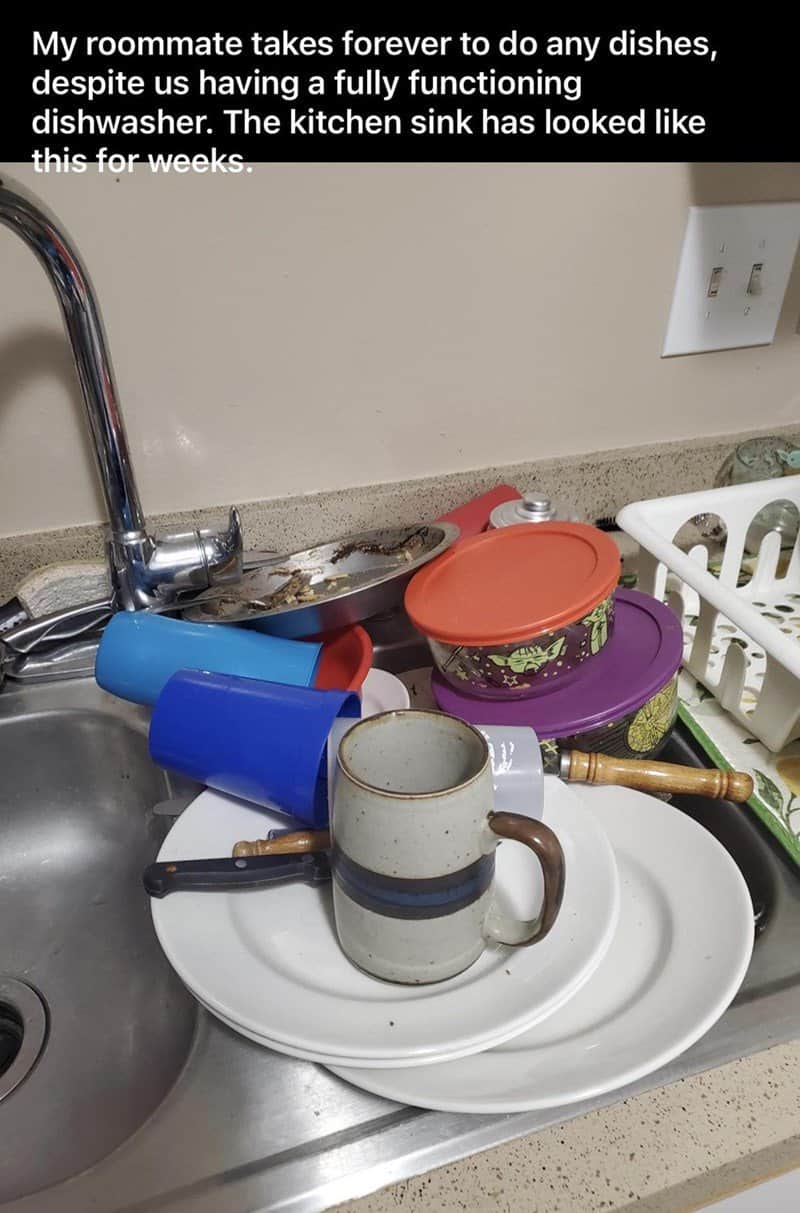 A kitchen nightmare caused by one of the worst roommates. A sink is piled high with a teetering mountain of dirty plates, blue plastic cups, and a ceramic mug that have reportedly been sitting there for weeks despite a working dishwasher.