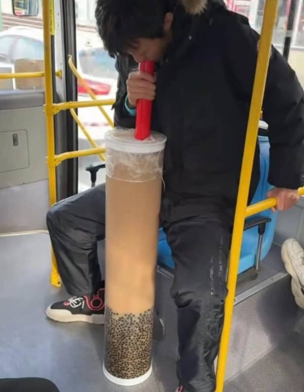 Person sitting on a bus drinking from a massive, floor-length container of boba tea.