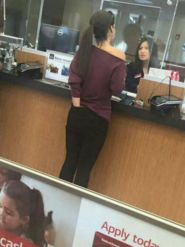 Woman at a bank counter reaching into her back pocket through a shirt hole.