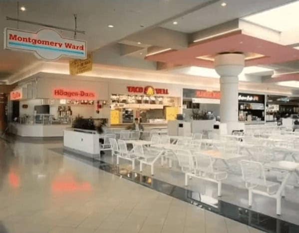 nostalgic 90s mall glamour shots view of a pristine food court. The shot features a classic neon "Häagen-Dazs" sign and the vintage yellow-and-red "Taco Bell" bell logo. The clean, white wire grid seating and pink geometric ceiling accents perfectly capture the peak mall aesthetic of the era.