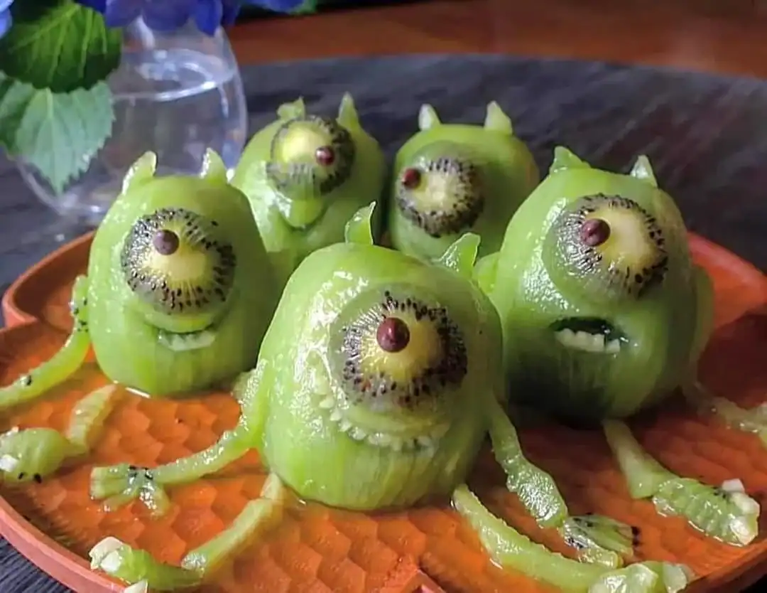 Creatively crafted fruit snacks made from peeled kiwis to look like the character Mike Wazowski from Monsters, Inc. Each kiwi features a single large eye made from a cross-section of another kiwi and a chocolate chip.