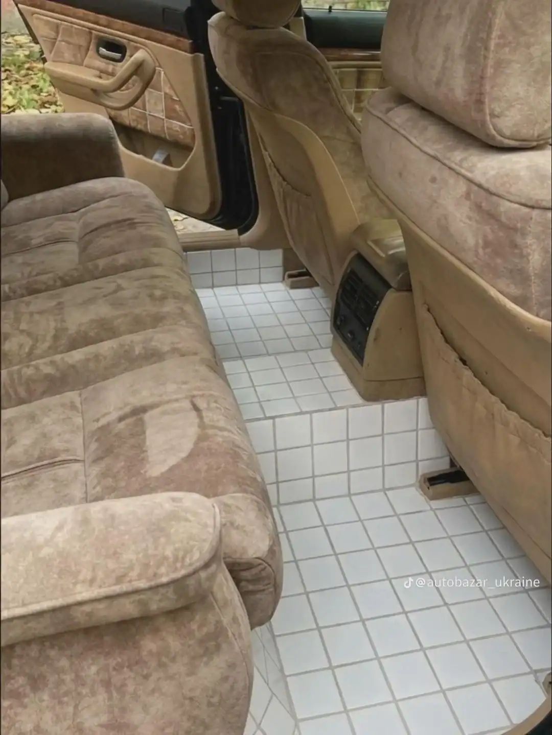 An interior car modification where the entire carpeted floor and footwells have been replaced with professionally installed, small white square bathroom tiles and dark grout.