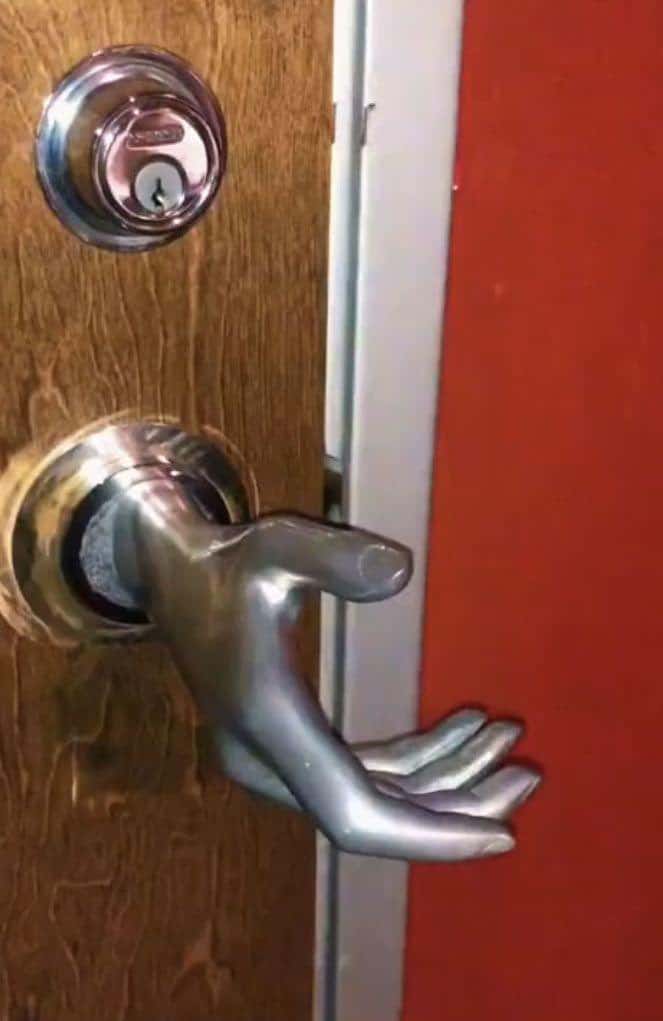 silver door handle sculpted into the shape of a realistic human hand reaching out from the wood. To enter the room, a person is forced to "shake hands" with the door to turn the latch.