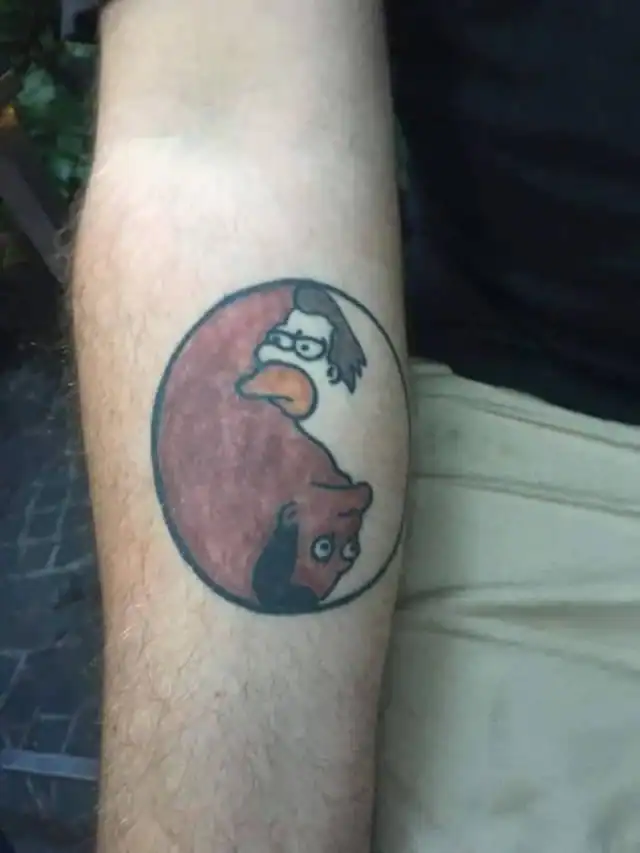 A clever but strange forearm tattoo of a Yin-Yang symbol formed by the opposing side-profiles of Homer Simpson and Ned Flanders from The Simpsons.