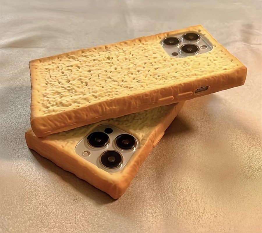 Two iPhones sporting hyper-realistic 3D cases sculpted to look like thick, porous slices of toasted sourdough bread, appearing crunchy enough to eat.