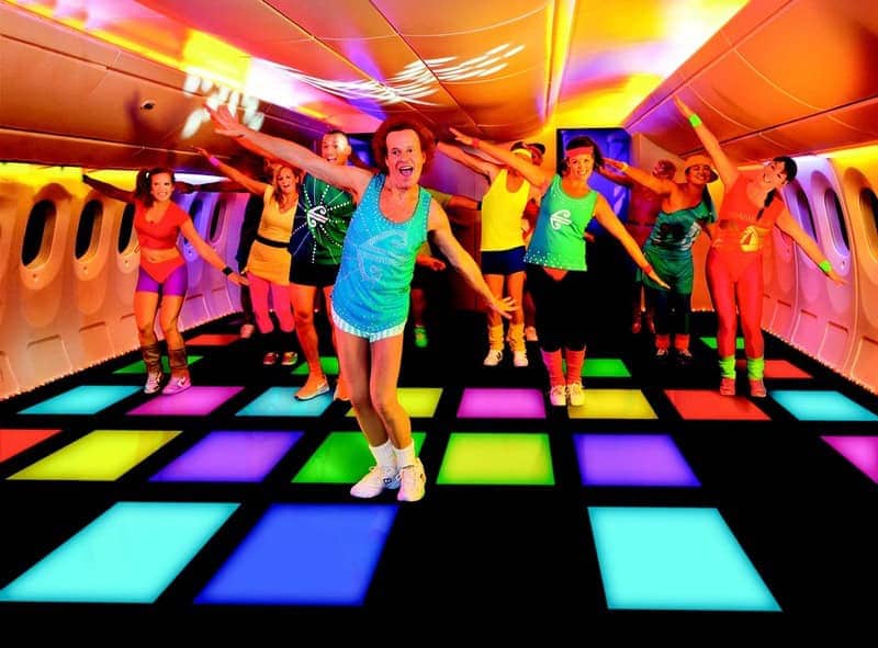 Energetic fitness instructor in sequined tank leads colorful group dance on LED floor