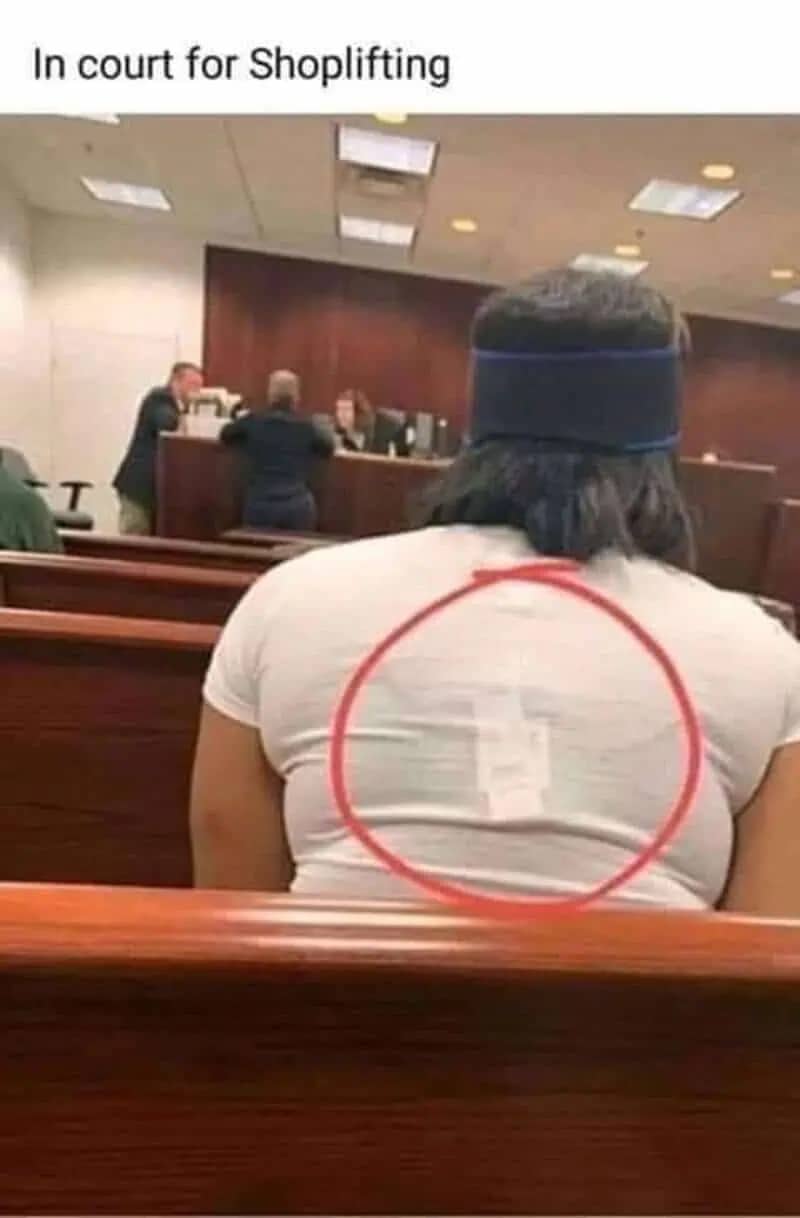 A shoplifting suspect in a courtroom with a security tag still attached to their white t-shirt.