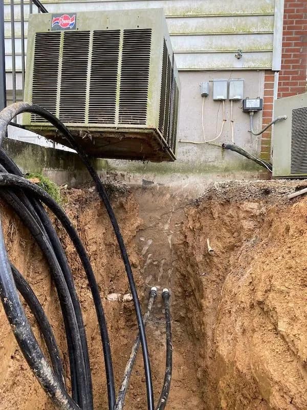 A gravity-defying funny picture of a massive commercial AC unit hanging in mid-air over a deep dirt trench after the ground beneath it was completely excavated.