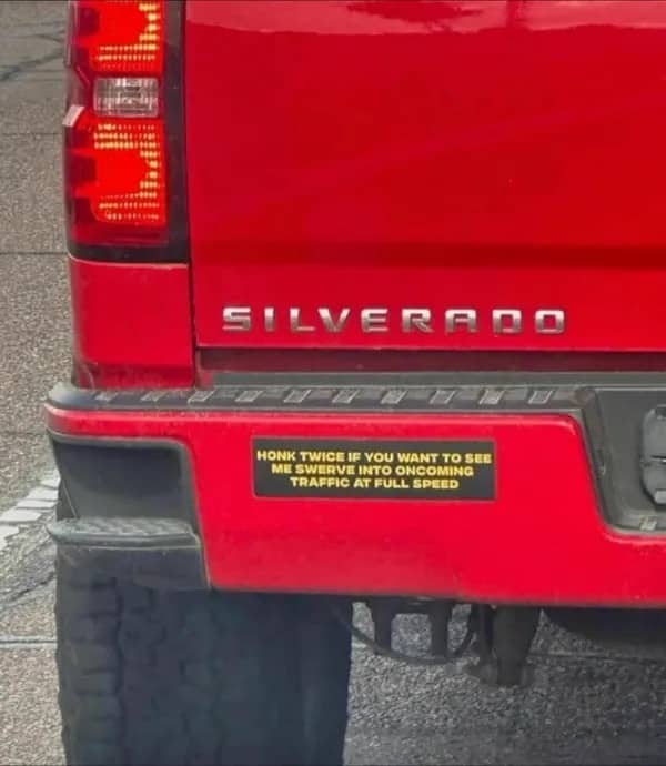 Red Chevrolet Silverado pickup truck with a dark humor bumper sticker about swerving into traffic.