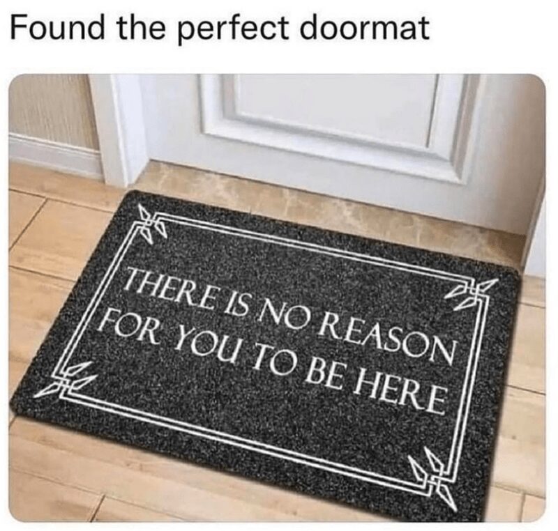 The ultimate introvert meme accessory: a black doormat with a crisp white border and formal serif text that bluntly states, "THERE IS NO REASON FOR YOU TO BE HERE."