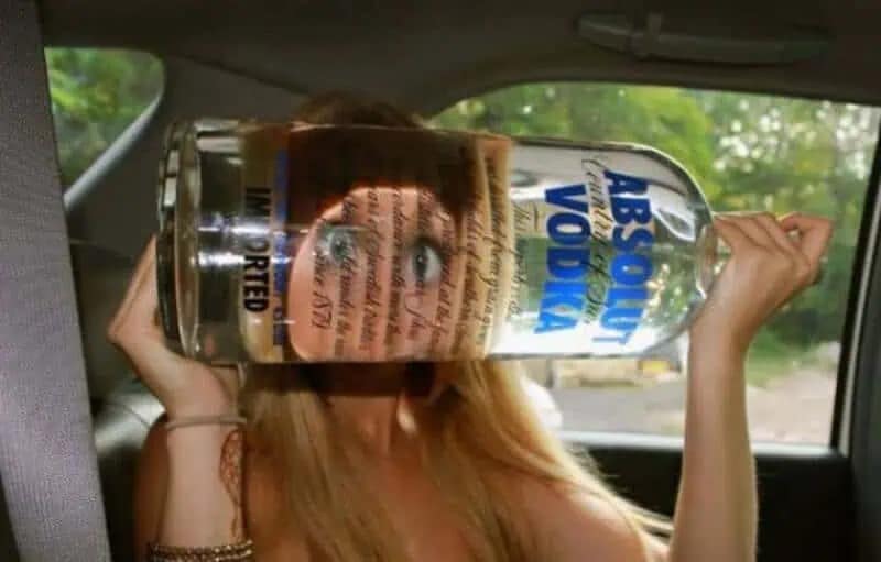 meme dump "drunk photography" image of a woman in a car holding a large bottle of Absolut Vodka horizontally against her face. Her eye is hilariously magnified to twice its size through the liquid in the bottle.