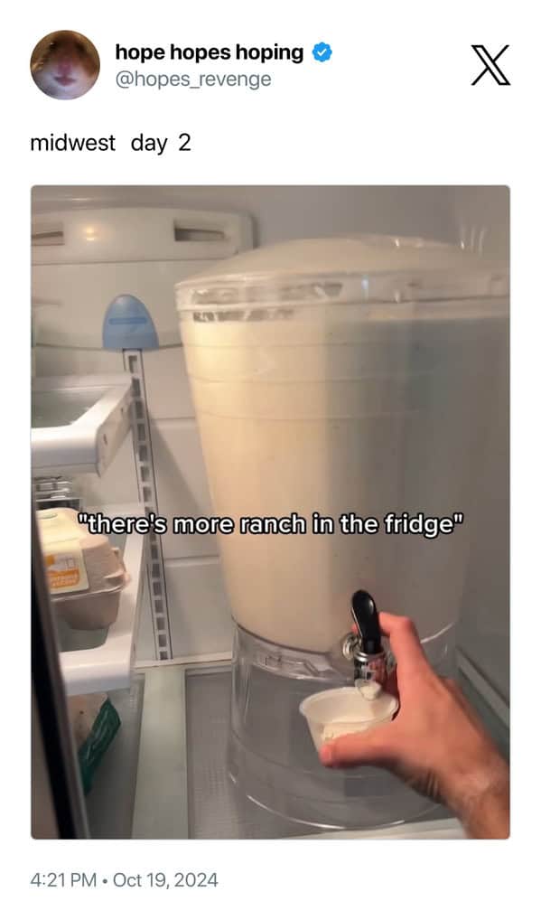 midwest meme showing a giant commercial beverage dispenser sitting on a refrigerator shelf, completely filled with ranch dressing. A hand is shown filling a small plastic cup from the spigot, captioned: "midwest day 2... 'there's more ranch in the fridge'."