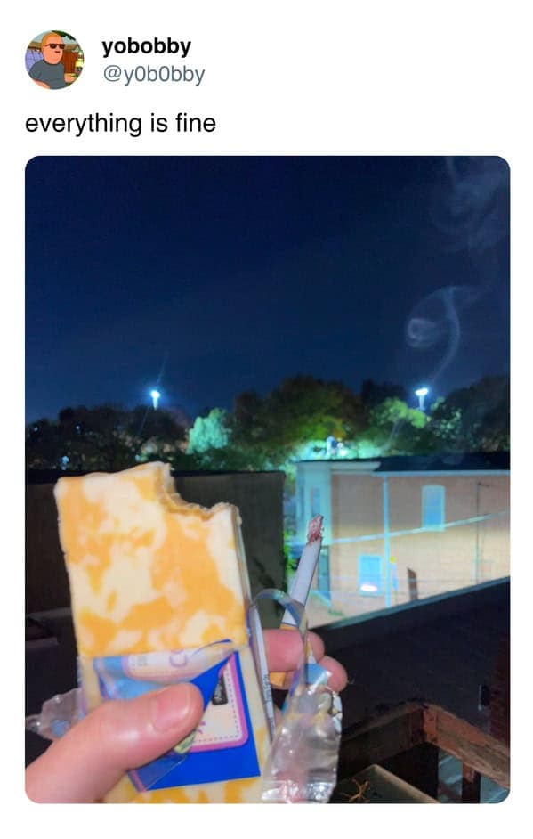 midwest meme from @y0b0bby. The photo shows someone standing on a balcony at night, holding a lit cigarette in one hand and taking a large bite out of a thick, vertical block of Colby-Jack cheese in the other. The caption reads: "everything is fine."