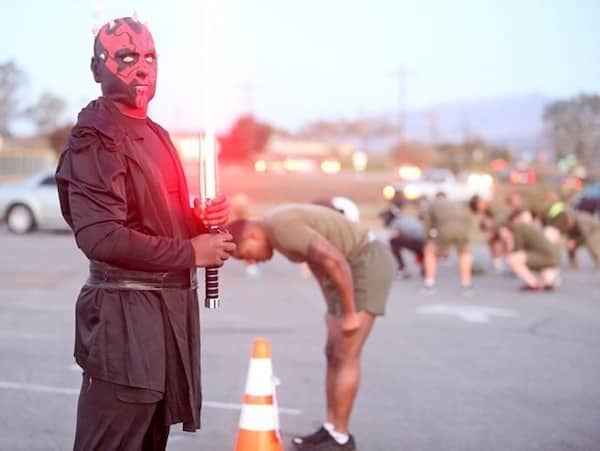 Drill instructor dressed as Darth Maul with lightsaber while soldiers do PT exercises in background