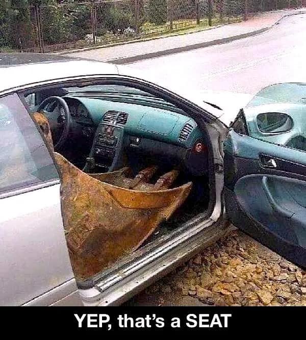 peak redneck DIY car modification where the passenger seat of a silver sedan has been replaced entirely by a rusted, heavy-duty excavator bucket. The jagged metal teeth of the bucket rest against the dashboard, perfectly matching the meme caption: "YEP, that’s a SEAT."