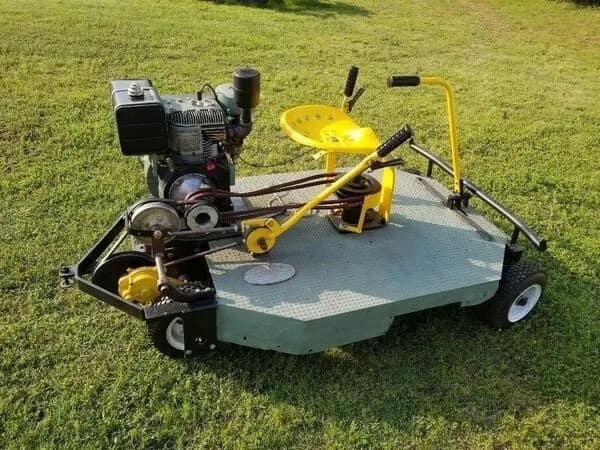 A terrifyingly efficient redneck DIY car consisting of a flat diamond-plate metal platform on wheels. It features a repurposed tractor seat, a small gas engine, and a complex series of exposed belt drives.