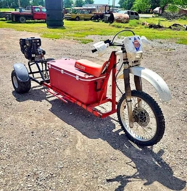 ultimate redneck DIY car for a summer tailgate: a custom motorized trike built around a massive red cooler. The front end is from a dirt bike, while the rear features a small industrial engine and a wide axle, allowing the driver to sit directly on the cooler lid.