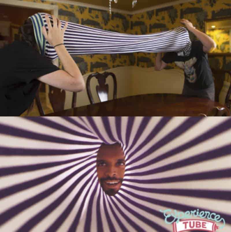 Two people stretching a striped Experience Tube with a man's face peering through the center