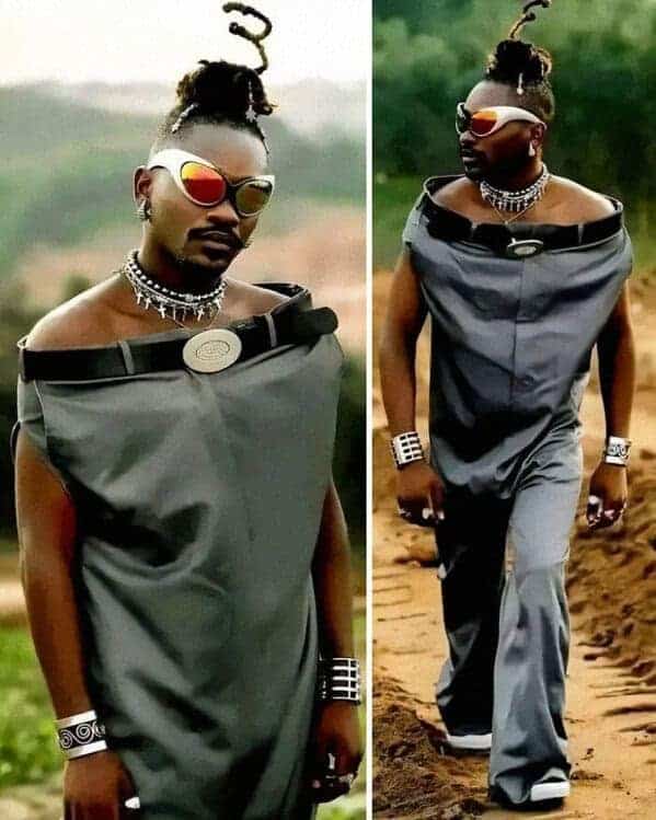 A viral weird fashion photo of a man wearing a pair of grey dress slacks as a top. He has pulled the waist of the pants up to his neck and secured a black leather belt around his collarbones, leaving his shoulders bare.