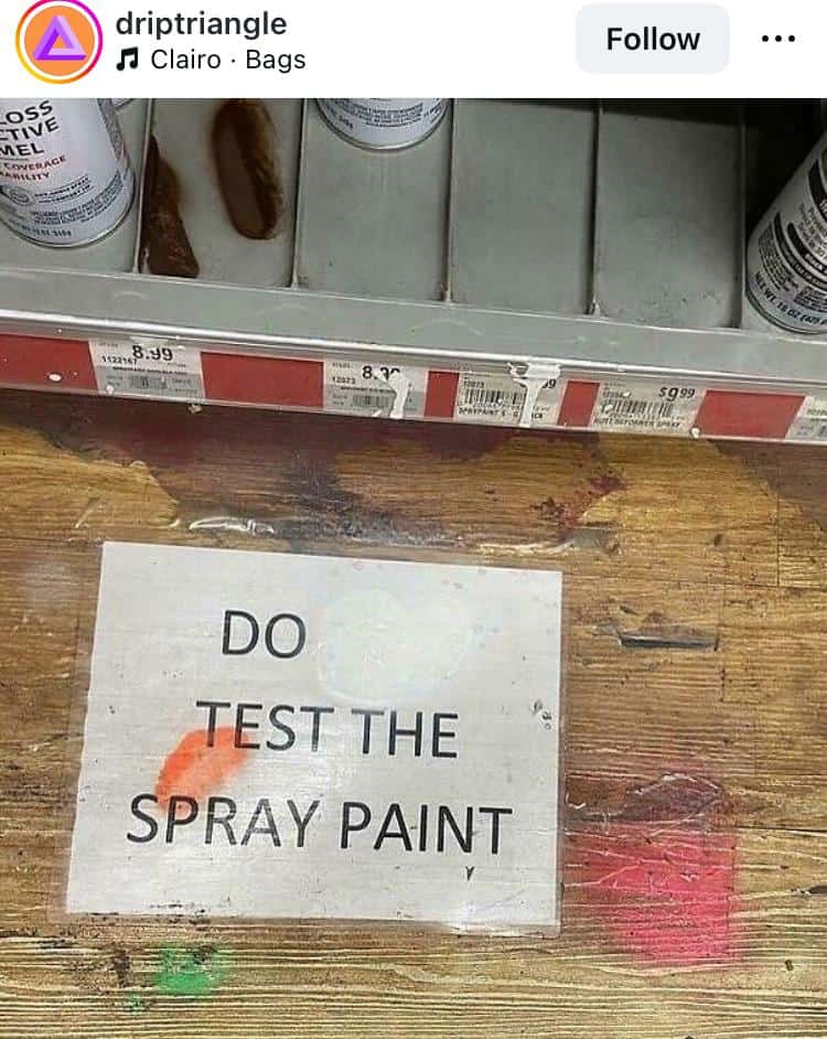 A subversive act of wholesome vandalism in a hardware store. A printed sign originally reading "DO NOT TEST THE SPRAY PAINT" has had the word "NOT" spray-painted over in white, now serving as a direct command: "DO TEST THE SPRAY PAINT."