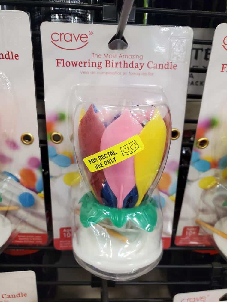 retail prank involving a "Flowering Birthday Candle" package. A yellow pharmacy sticker that reads "FOR RECTAL USE ONLY" has been applied to the plastic casing, creating a terrifying and highly inappropriate medical warning for a party supply.
