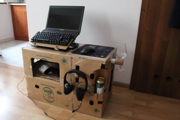 Laptop gaming station built entirely from cardboard boxes with cat hiding inside underneath