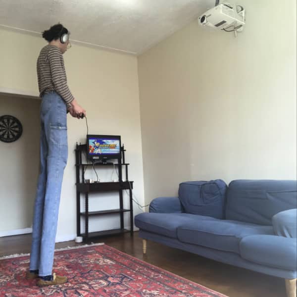 Person standing and gaming on tiny TV while projector hangs unused from ceiling above