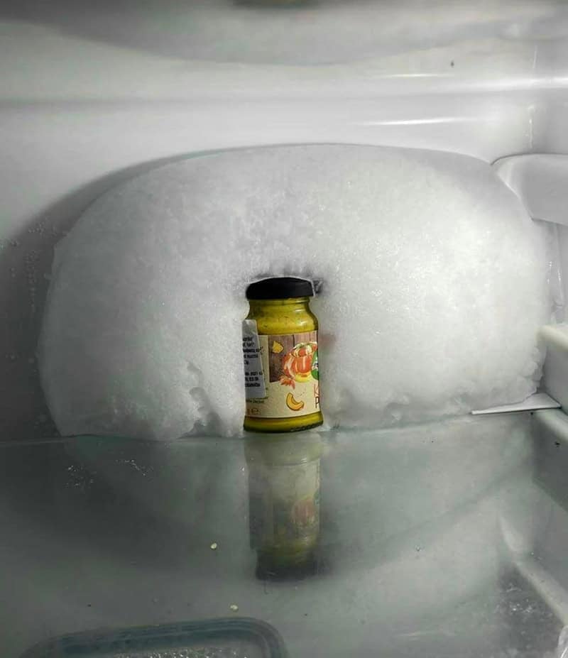 Neglected office freezer with massive ice buildup completely encasing lone sauce jar inside