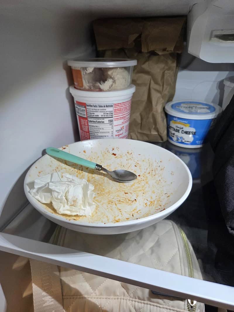 Dirty food-stained bowl with used spoon and crumpled napkin stored uncleaned inside office fridge