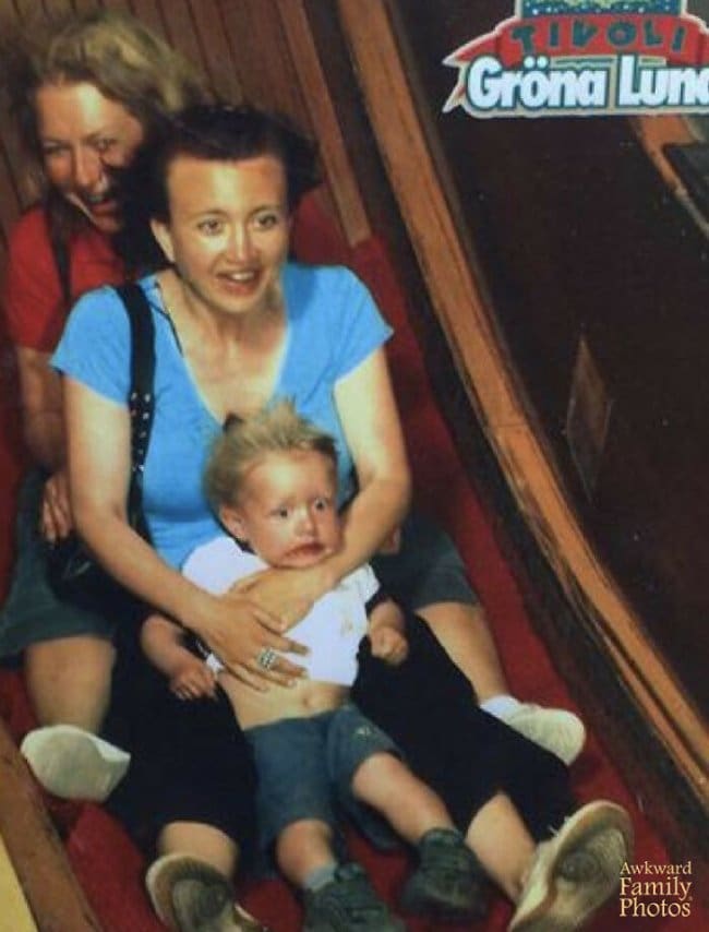 A toddler with wide, terrified eyes being held by his mother on a fast amusement park slide.